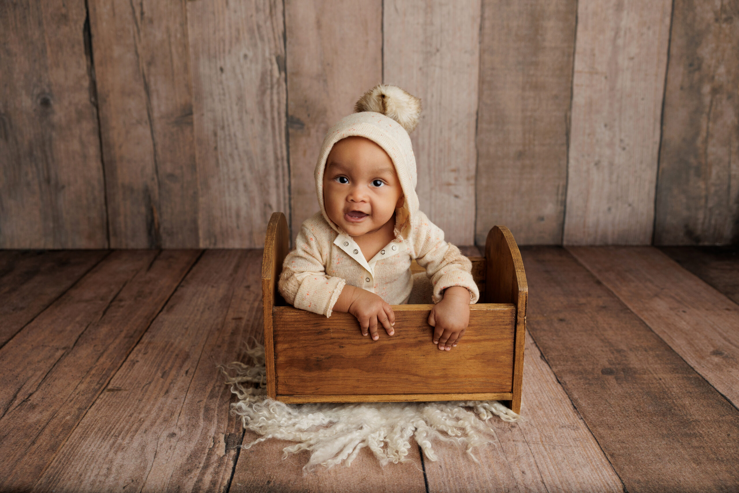 Sitting baby inside a small wooden prop wearing a romper with a hood for a North Hollywood Photography studio.