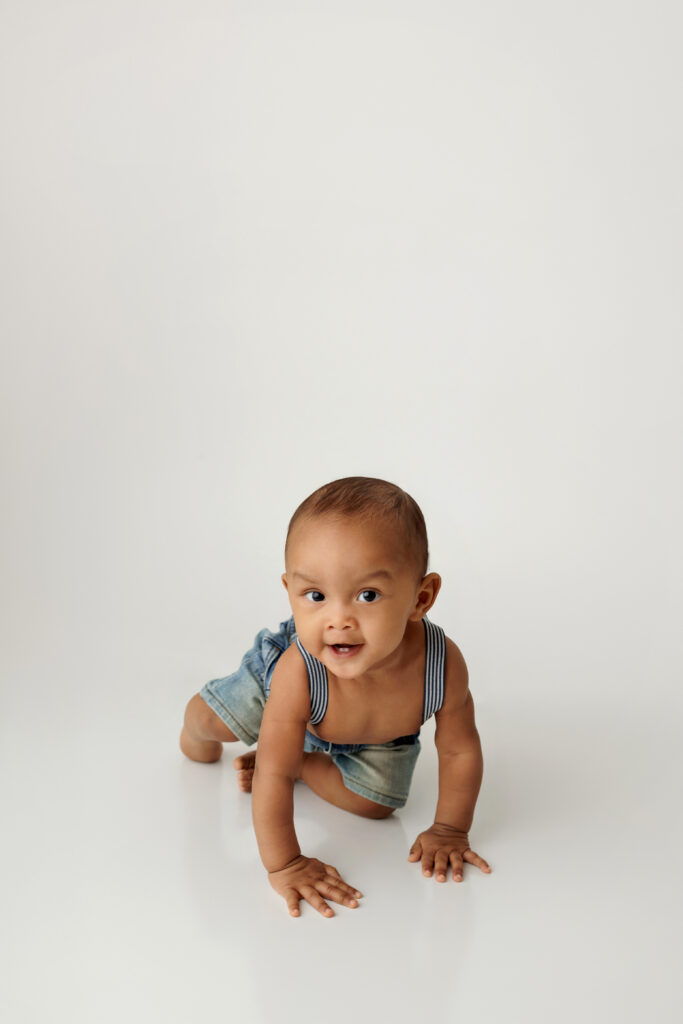 Baby wearing only overalls crawling on a white backdrop at a North Hollywood Photography studio