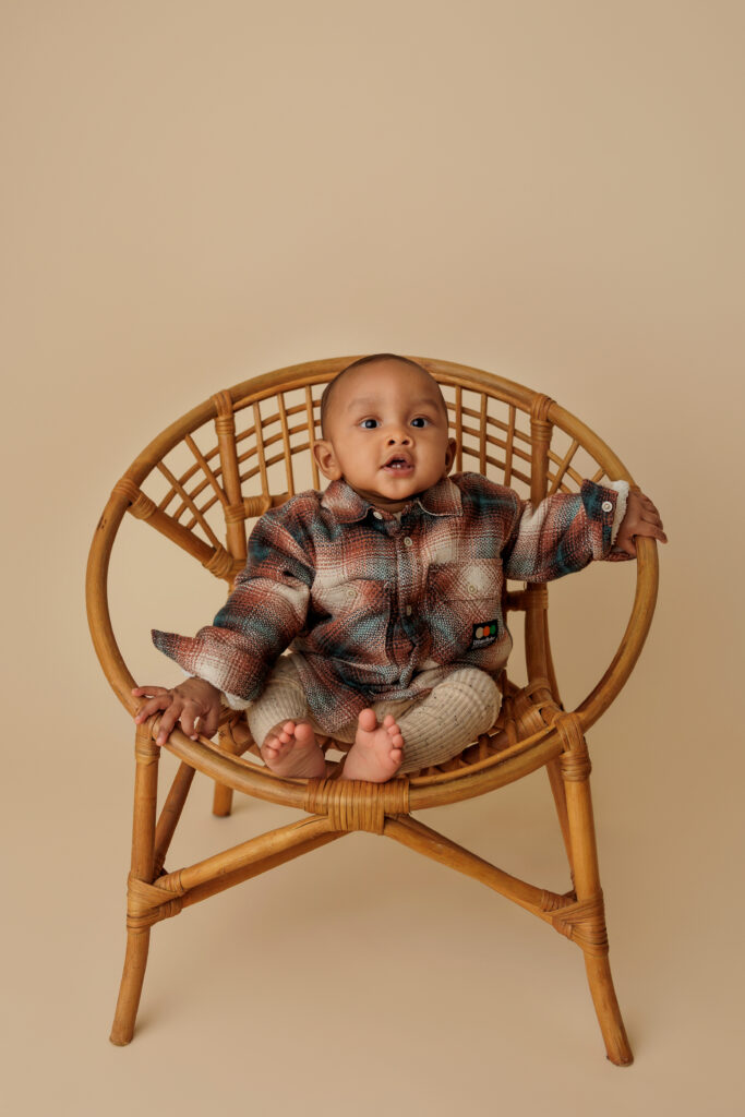 Baby sitting in a papasan chair in a multi colored flannel