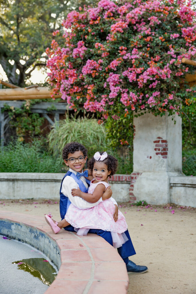 two siblings in an outdoor setting, surrounded by foliage